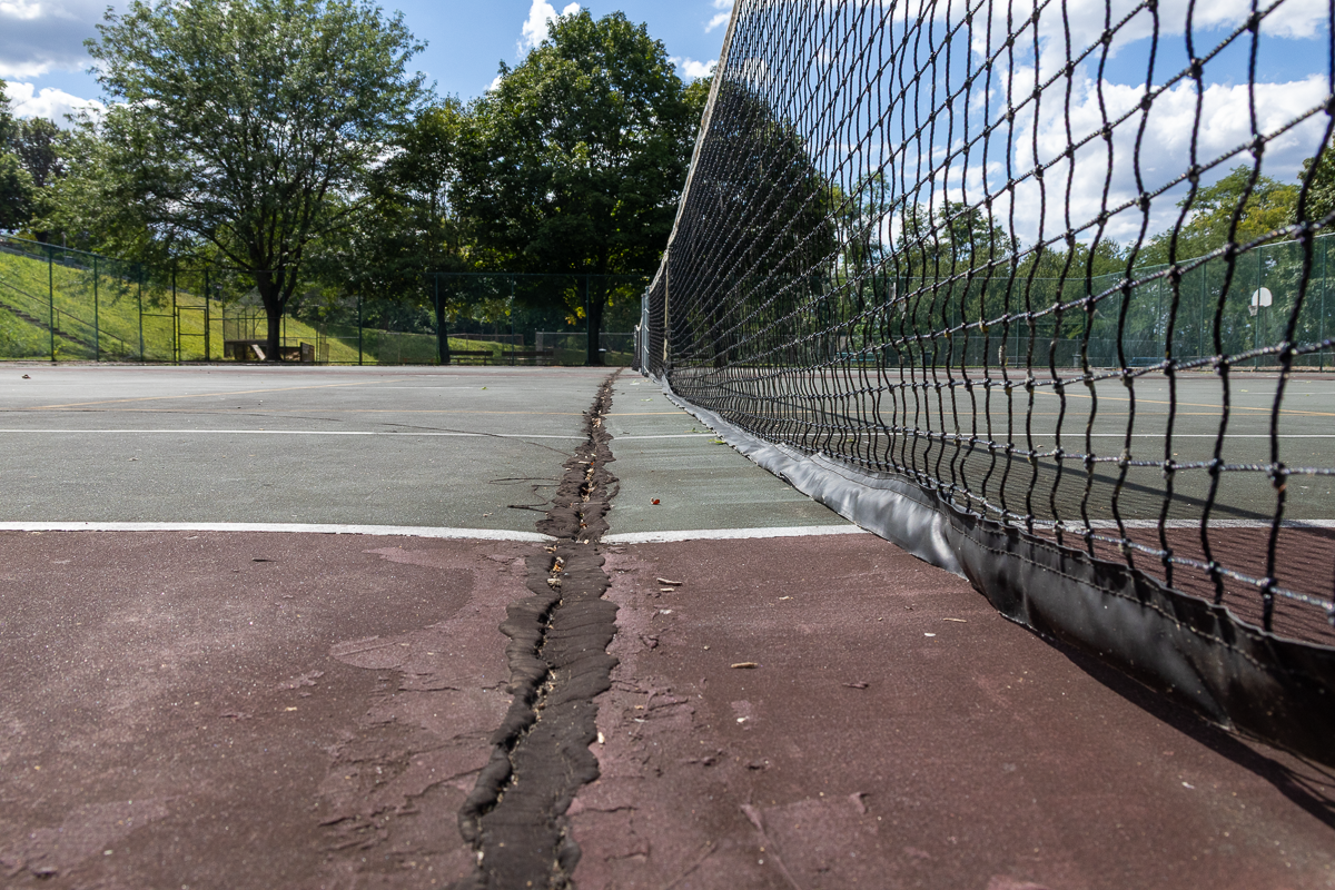 Close up view of a large crack in the middle of a damaged tennis court.