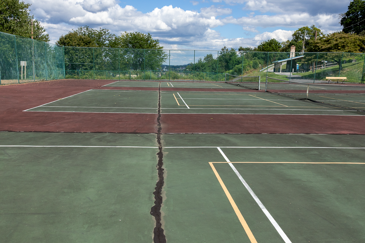 Aerial view of a damaged tennis court with a large crack down the center.